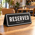 Black 3D printed Reserved table sign on a wooden café table