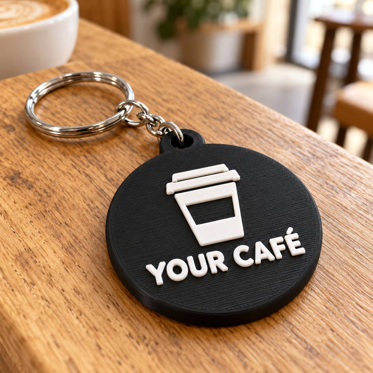 Round black 3D printed keyring with takeaway coffee cup logo and café name on a wooden table