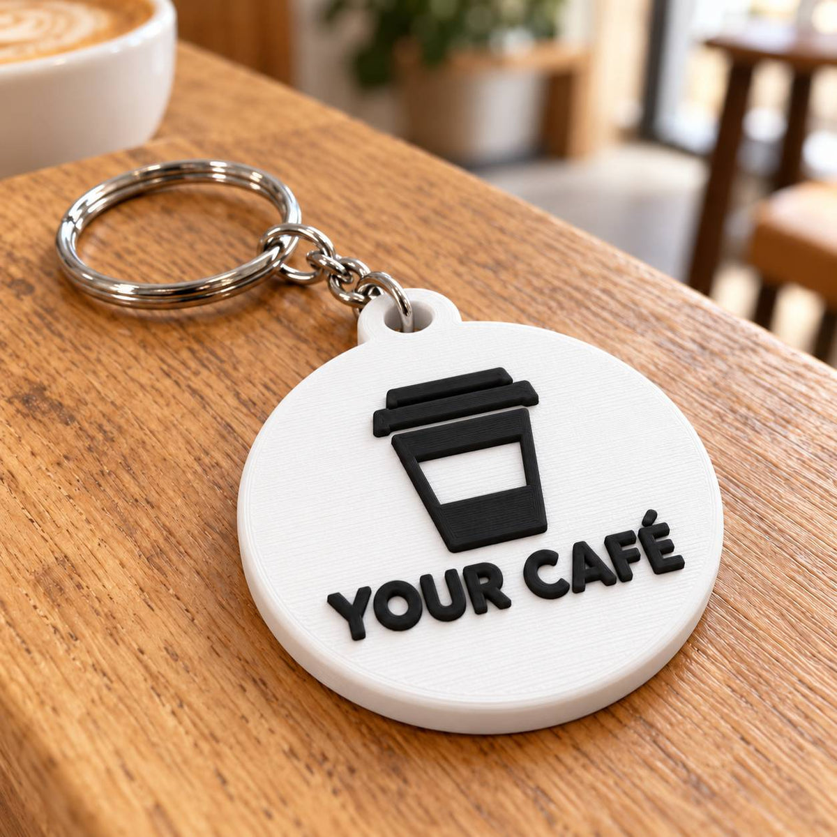 Round white 3D printed keyring with takeaway coffee cup logo and café name on a wooden table